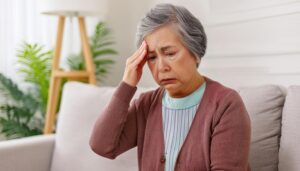 ソファで頭痛を感じる高齢女性