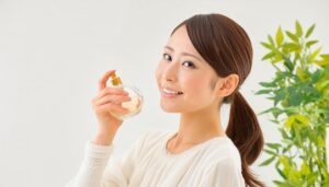観葉植物を背景に香水を持つ女性の笑顔