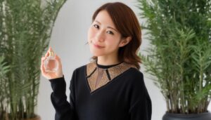 観葉植物に囲まれ香水を持つ30代女性の笑顔