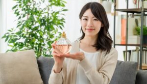 ベージュカーディガン女性が丸い香水を両手で持つ