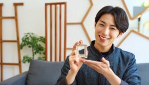 紺色のジャケットで香水ボトルを両手で支える笑顔の男性
