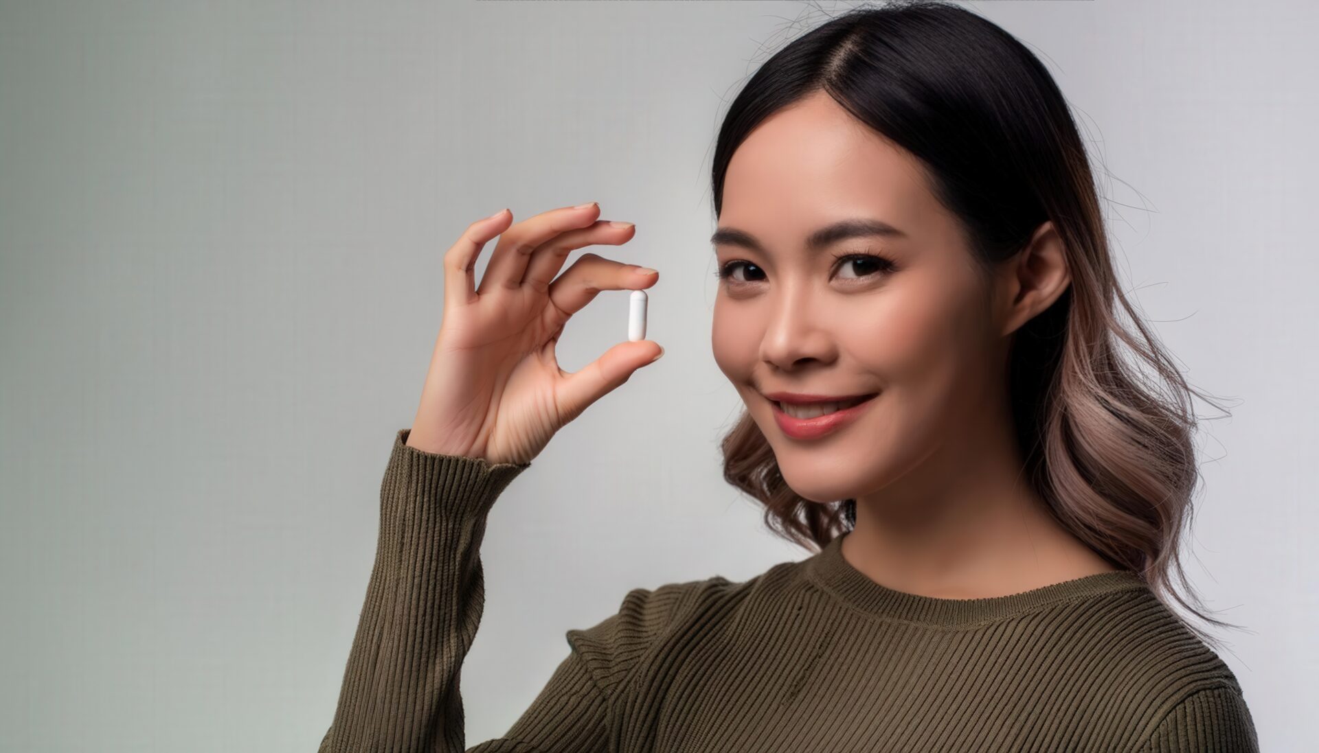 オリーブ色のトップスで白いカプセルを手にする人物
