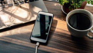 コーヒーカップとノートPCのそばで充電中のスマホ