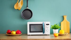 青緑の壁に置かれた白い電子レンジとフライパン