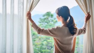 窓辺でカーテンを開ける若い女性