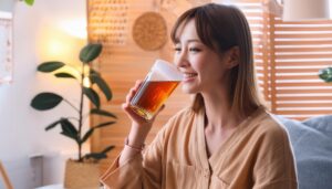 明るい室内でグラスの茶色い飲み物を飲む若い人