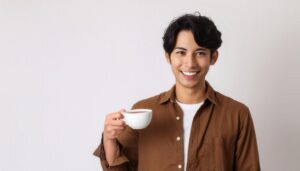 白背景で白いカップの茶色い飲み物を持つ若い人