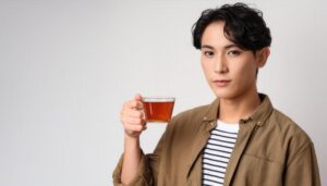 白背景で透明カップの茶色い飲み物を持つ若い人