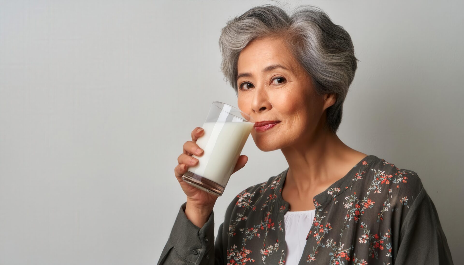 白背景で牛乳を飲むシニア女性（花柄の服）