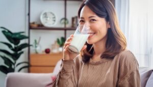 室内で牛乳を飲む若い女性（ブラウンのトップス）