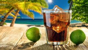 ビーチを背景にライムを添えた黒い炭酸飲料のグラス