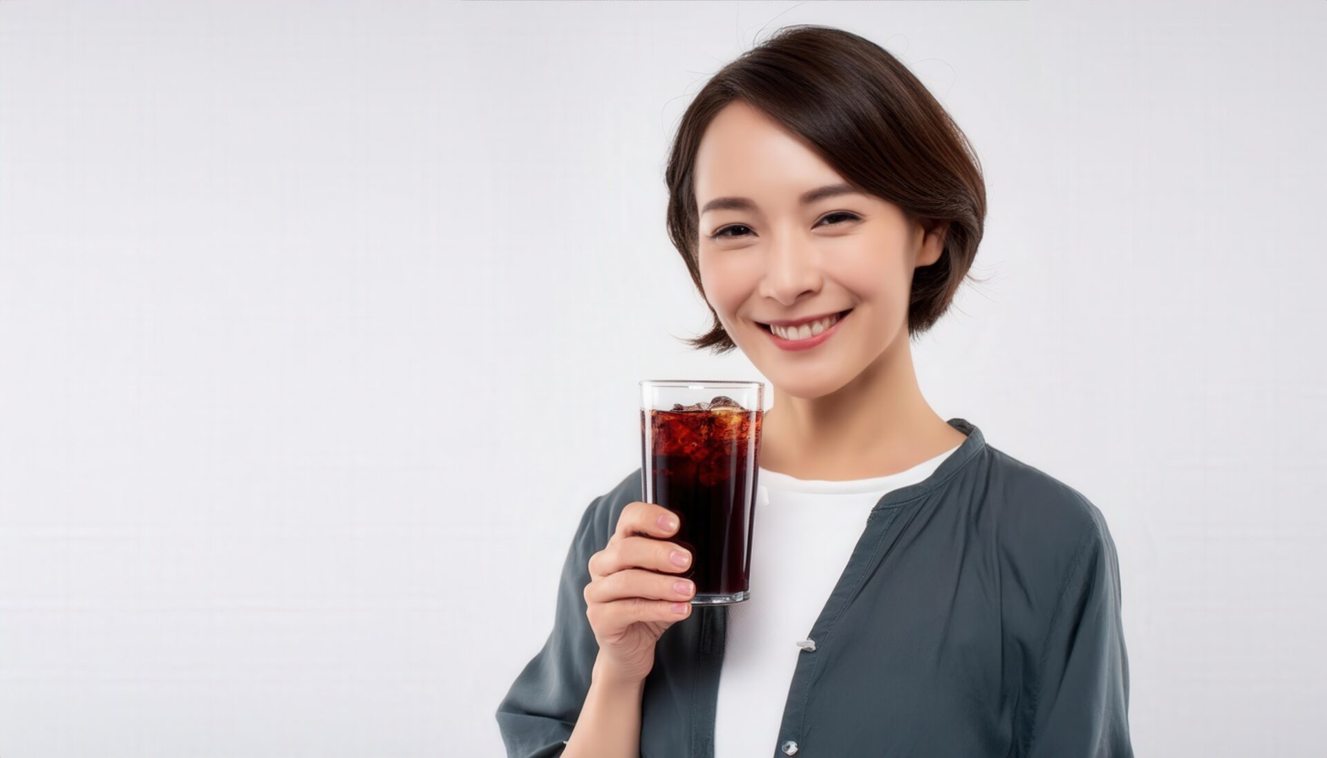 白背景で黒い炭酸飲料のグラスを手に持つ若い女性