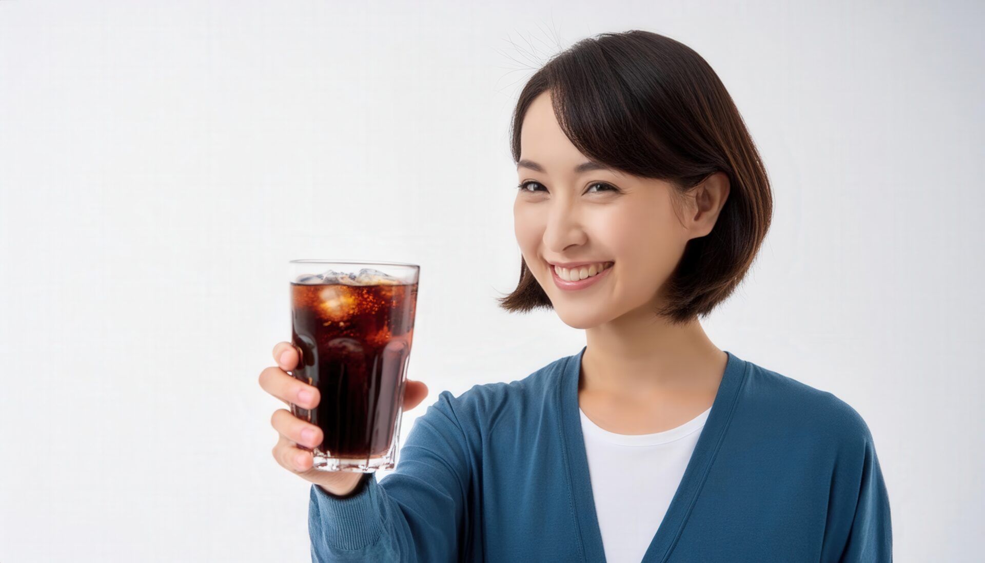 白背景で黒い炭酸飲料のグラスを差し出す若い女性