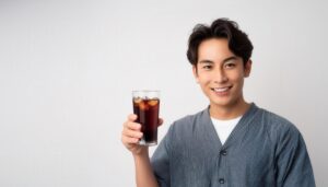 白背景で黒い炭酸飲料のグラスを手に持つ若い男性