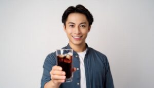 白背景で黒い炭酸飲料のグラスを手に持つ若い男性