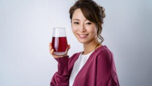 グレー背景で赤紫色のグレープジュースを持つ若い女性
