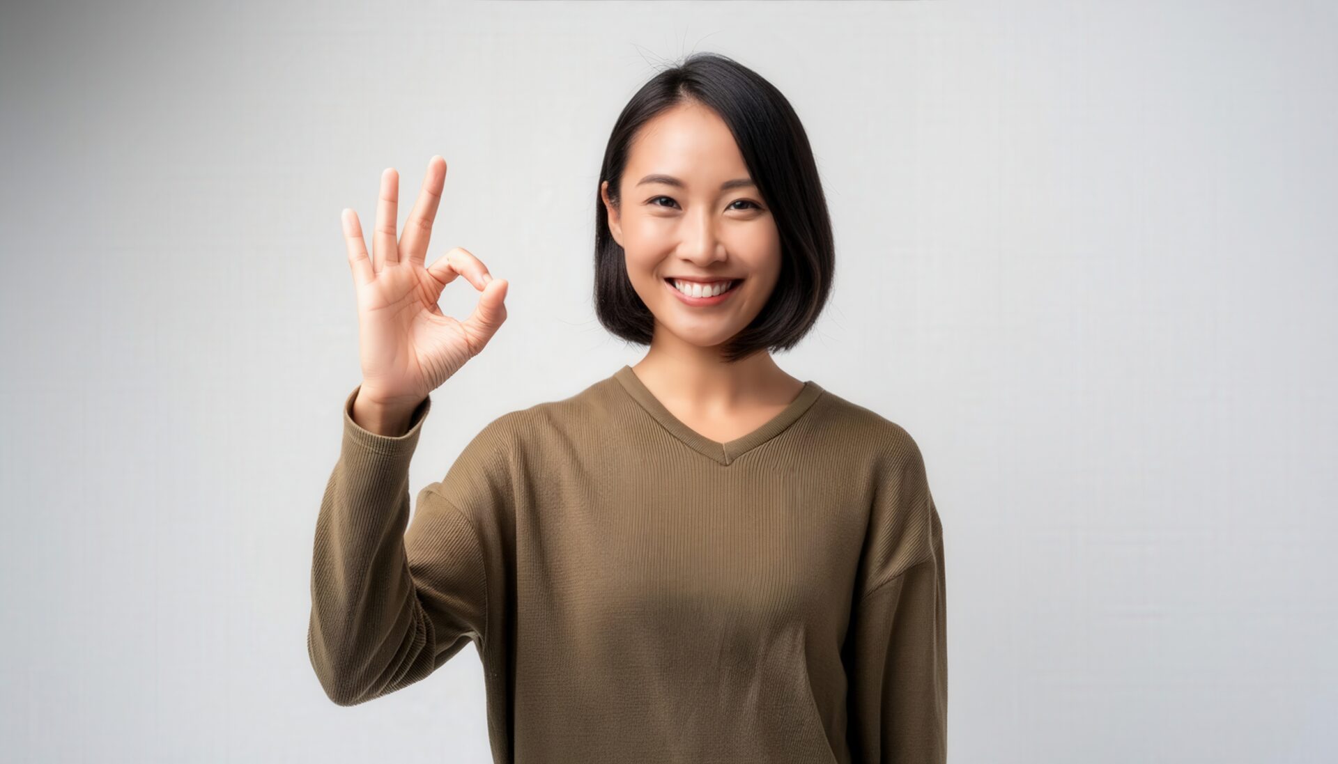 白背景でOKサインをするショートヘアの人物