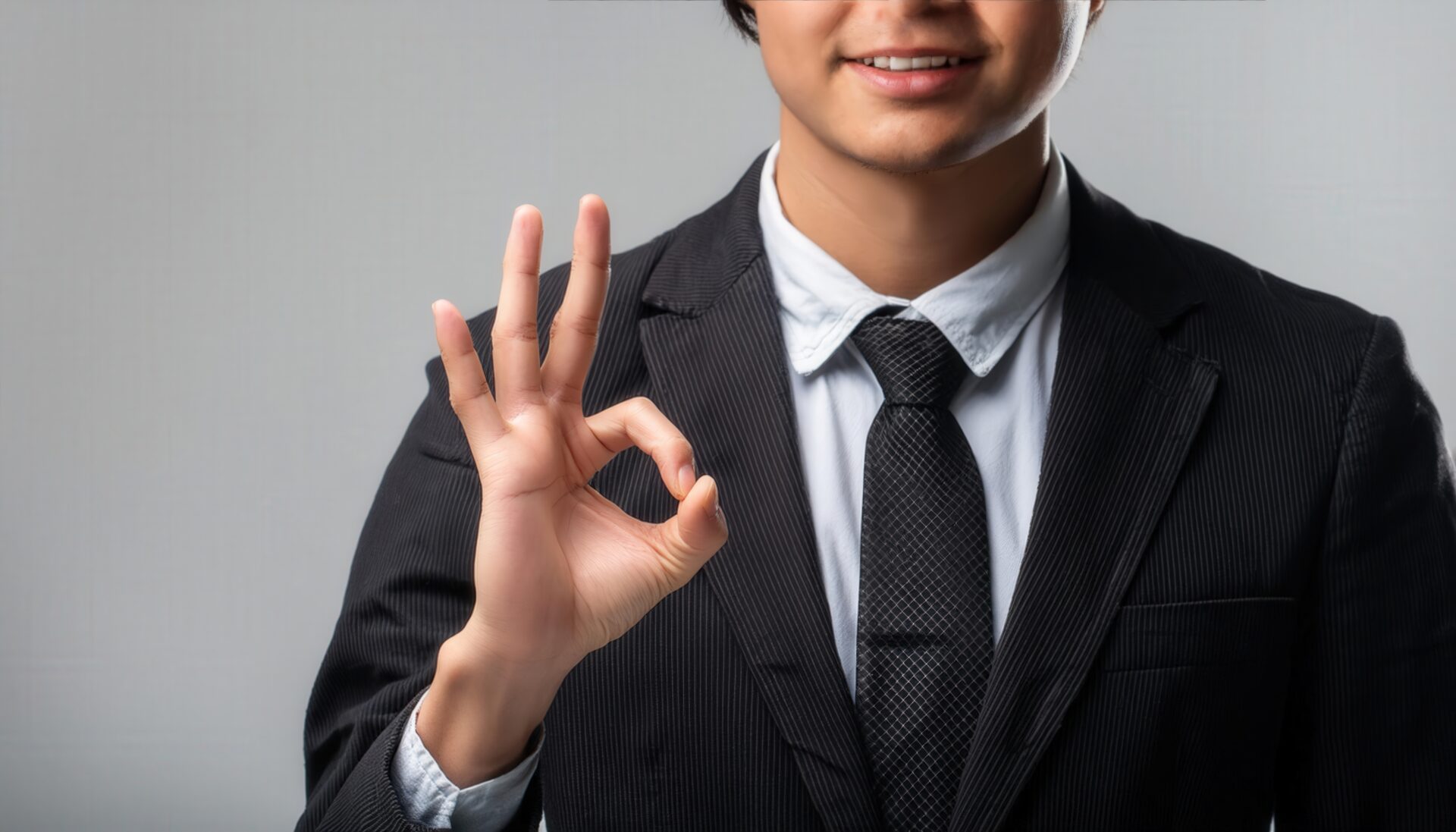 グレー背景でスーツ姿の人物がOKサイン