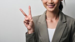 白背景でスーツ姿の人がピースサインをしている（部分カット）