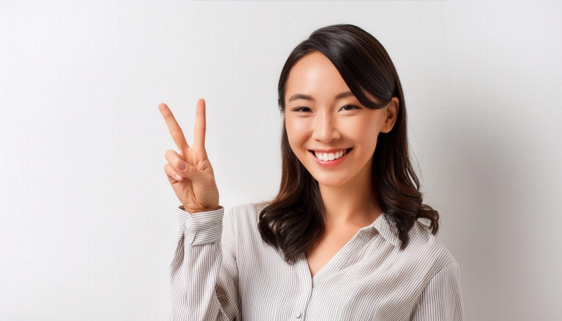 白背景でカジュアルな装いの人がピースサインをしている