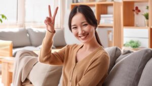 室内のリビングで笑顔でピースサインをする女性