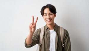 白背景でリュックを背負った若い男性がピースサインをしている