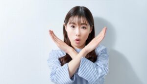 白背景で腕をクロスして拒否を示す人物