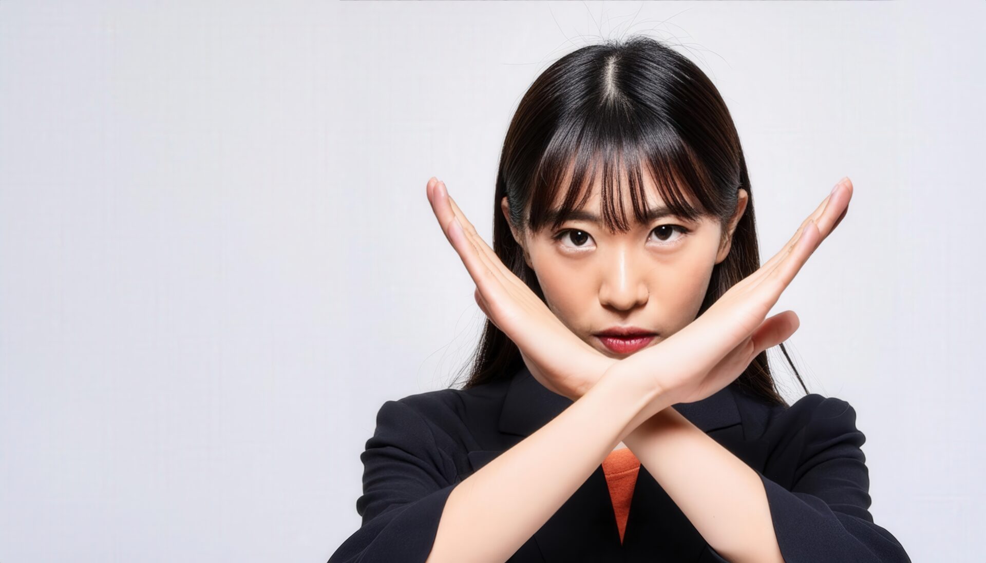 白背景でクロスサインを出すビジネスウェアの女性