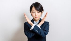 白背景で腕をクロスしてNGを伝えるスーツの女性