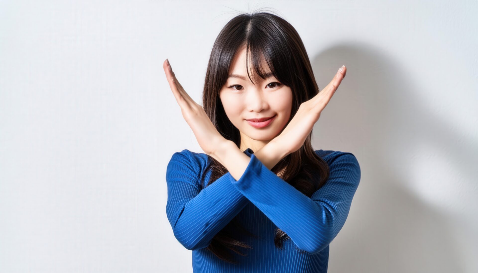 白背景で青い服を着て腕をクロスしてNGサインを示す人