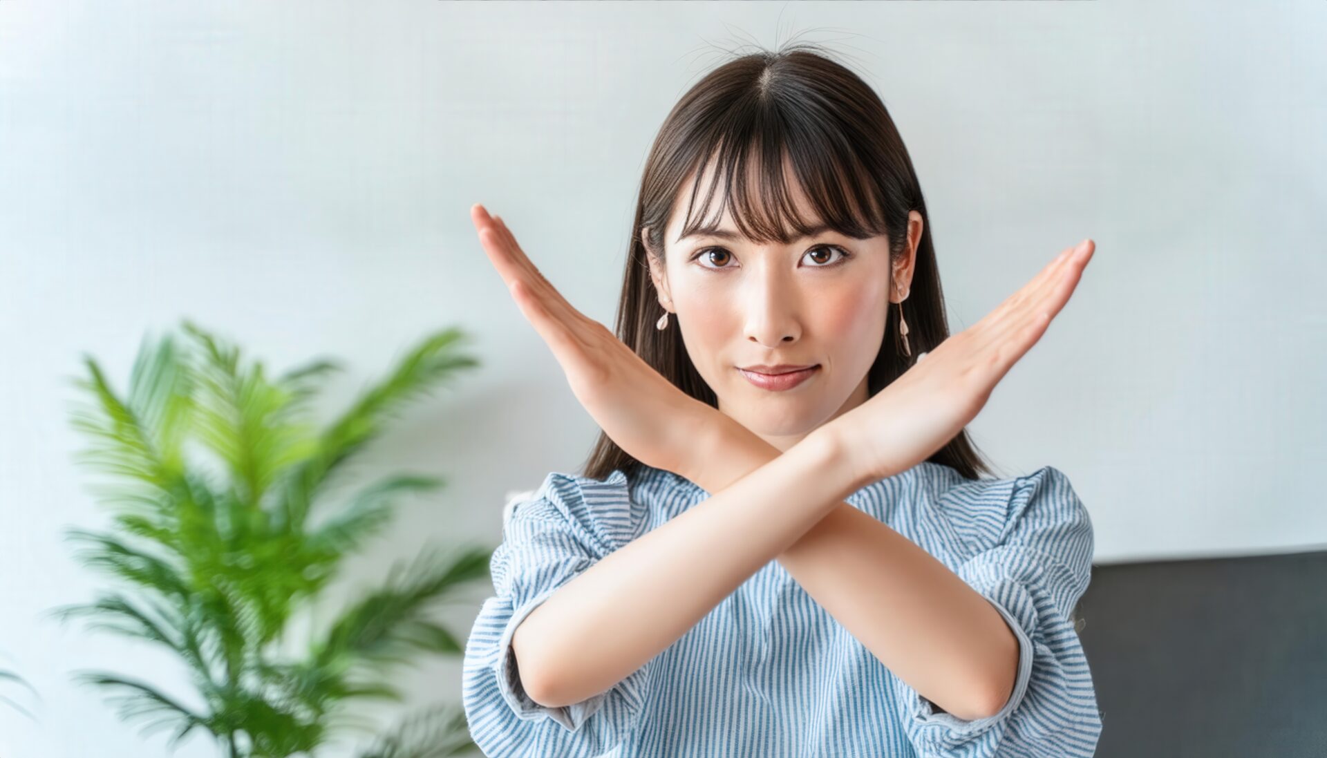 室内でストライプ柄の服を着て腕をクロスしてNGサインを示す人