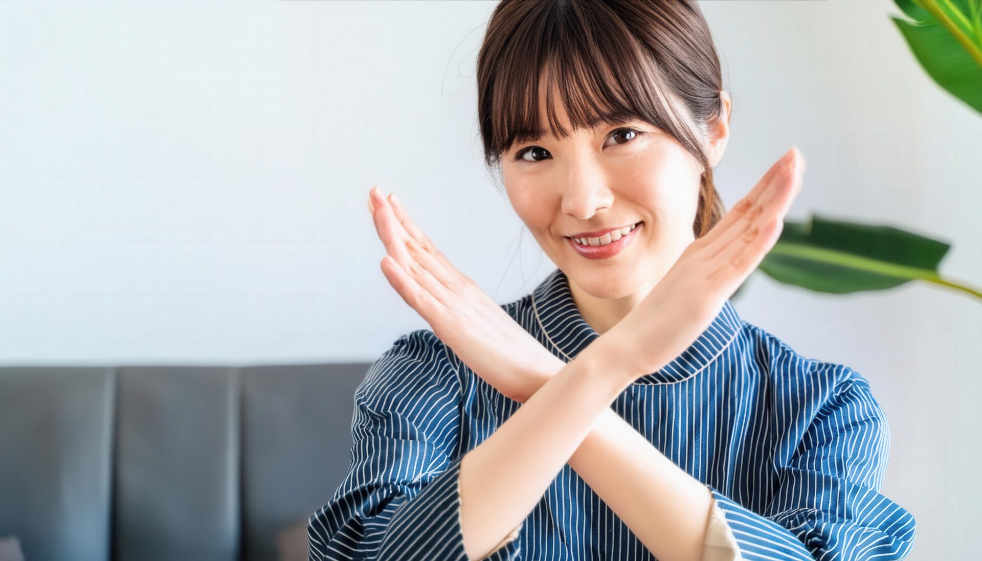 室内でストライプシャツを着て腕をクロスしてNGサインを示す人