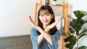 室内でチェック柄のトップスを着て腕をクロスしてNGサインを示す人