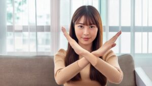 室内でベージュのトップスを着て腕をクロスしてNGサインを示す人