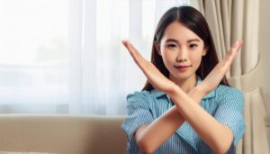 室内でストライプのシャツを着て腕をクロスしてNGサインを示す人