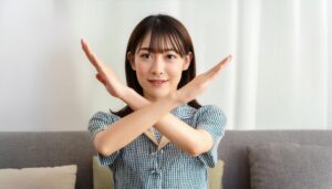 室内でギンガムチェックの服を着て腕をクロスしてNGサインを示す人