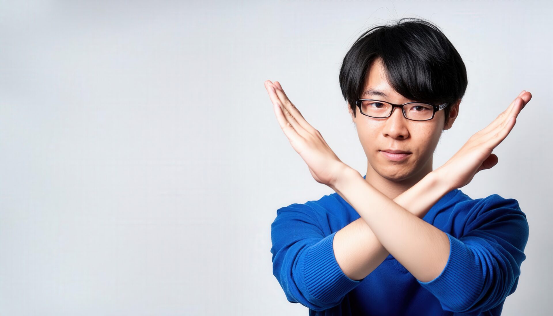 白背景で青いトップスを着て腕をクロスしてNGサインを示す人