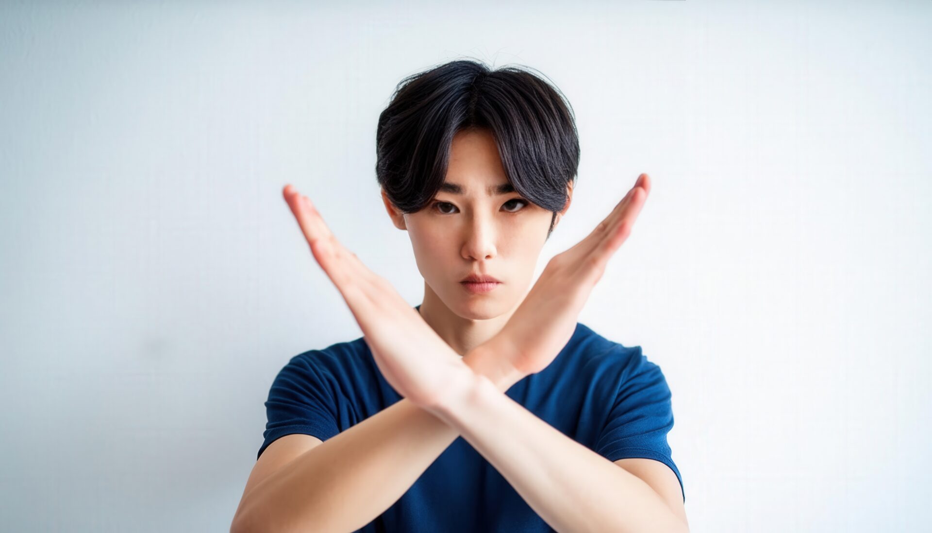 白背景で青いTシャツを着て腕をクロスしてNGサインを示す人