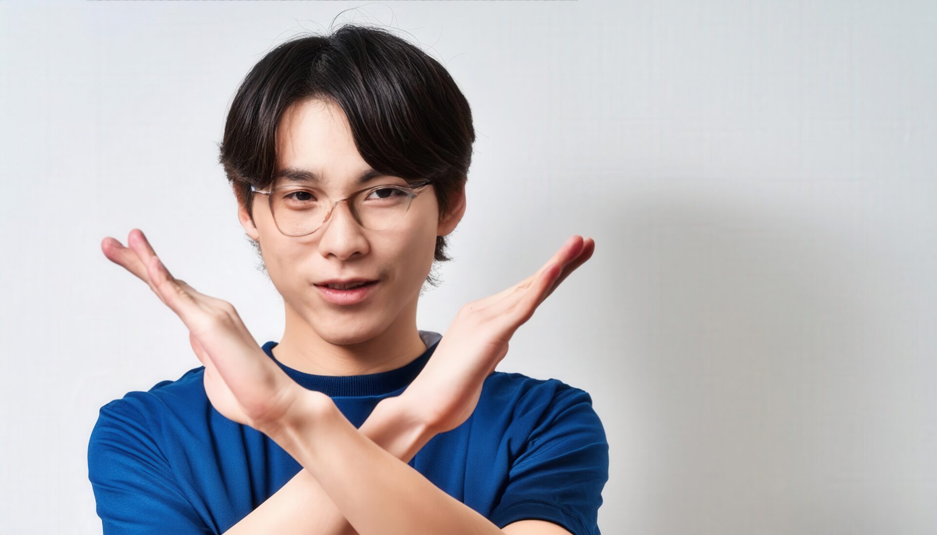 白背景で青いTシャツとメガネをかけて腕をクロスしてNGサインを示す人
