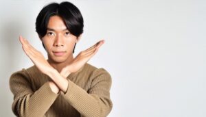 白背景でベージュのトップスを着て腕をクロスしてNGサインを示す人