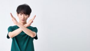 白背景でグリーンのTシャツを着て腕をクロスしてNGサインを示す人