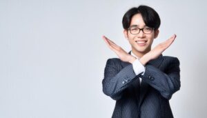 白背景でストライプのスーツを着てメガネをかけて腕をクロスしてNGサインを示す人