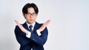 白背景でメガネと青いスーツを着て腕をクロスしてNGサインを示す人