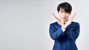 白背景で青いスーツを着て腕をクロスしてNGサインを示すビジネスパーソン