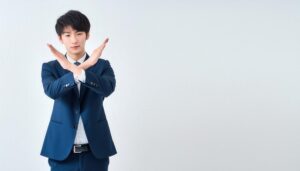 白背景で青いスーツ姿で腕をクロスしてNGサインを示す人