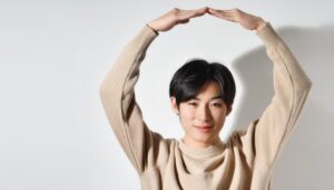 ベージュのセーターで頭上に円を作っている若い人