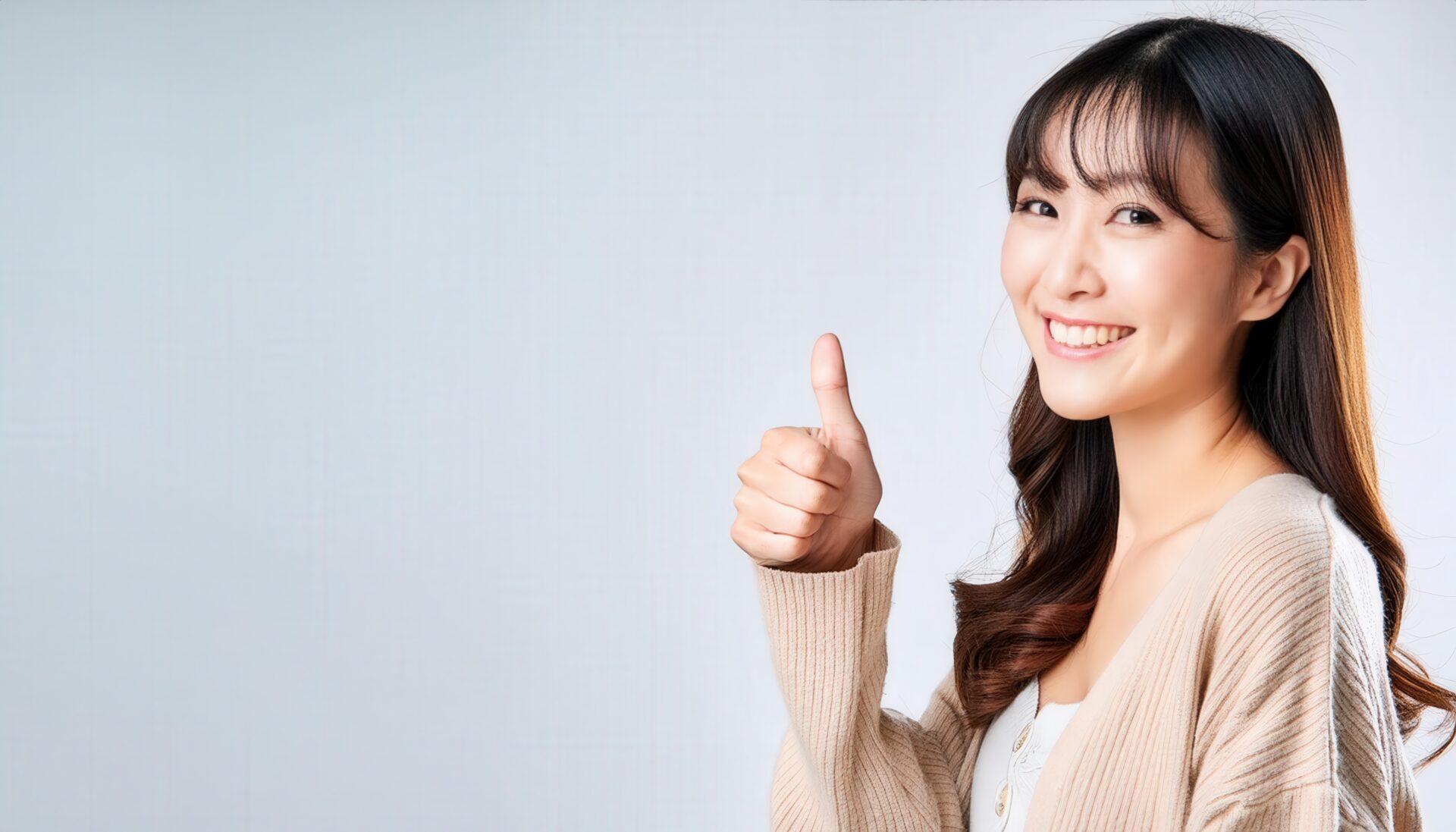 ベージュのカーディガンでグッドサインをしている若い人