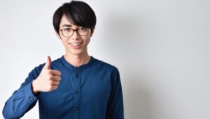 メガネをかけた若い男性が親指を立てるポートレート