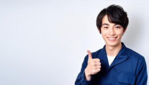 白背景でブルーの作業服を着た若者がサムズアップ
