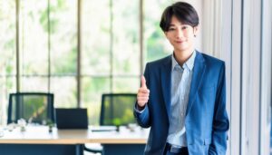 大きな窓のあるオフィスで親指を立てるビジネスパーソン